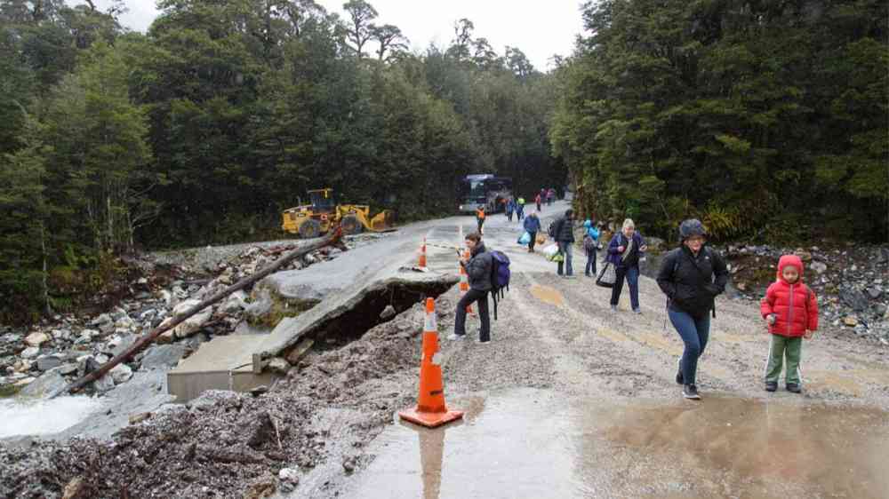 Tourists traverse the side of a road eroded by floods in Doubtful Sound, New Zealand