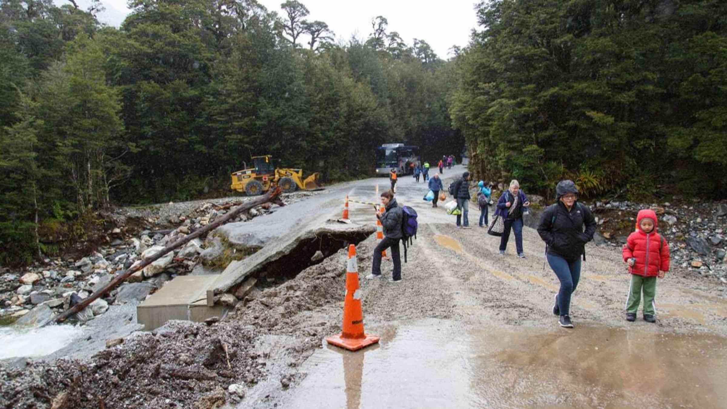 Tourists traverse the side of a road eroded by floods in Doubtful Sound, New Zealand