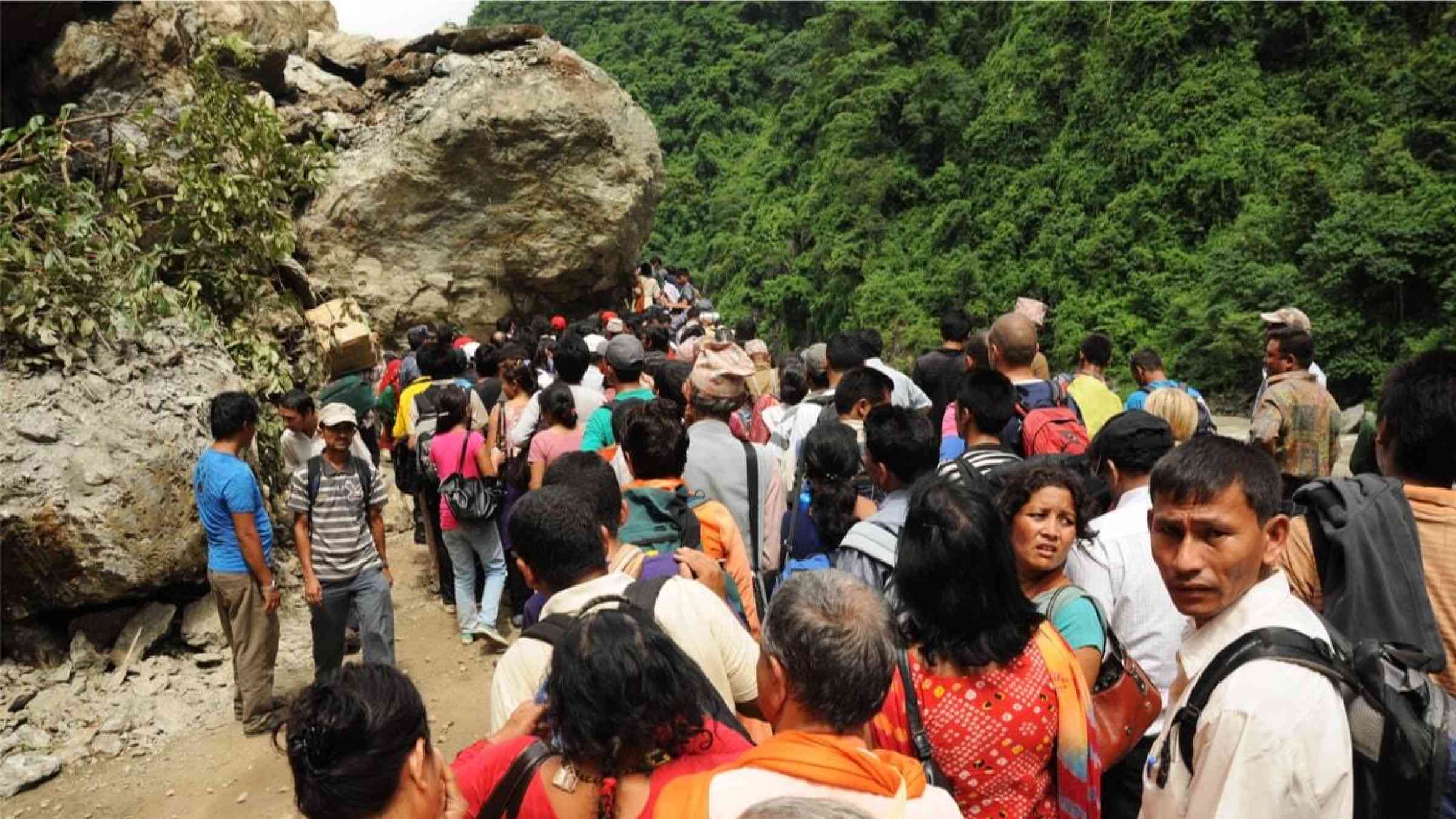 Nepalis wait as engineers remove a boulder fallen on the road due to a landslide