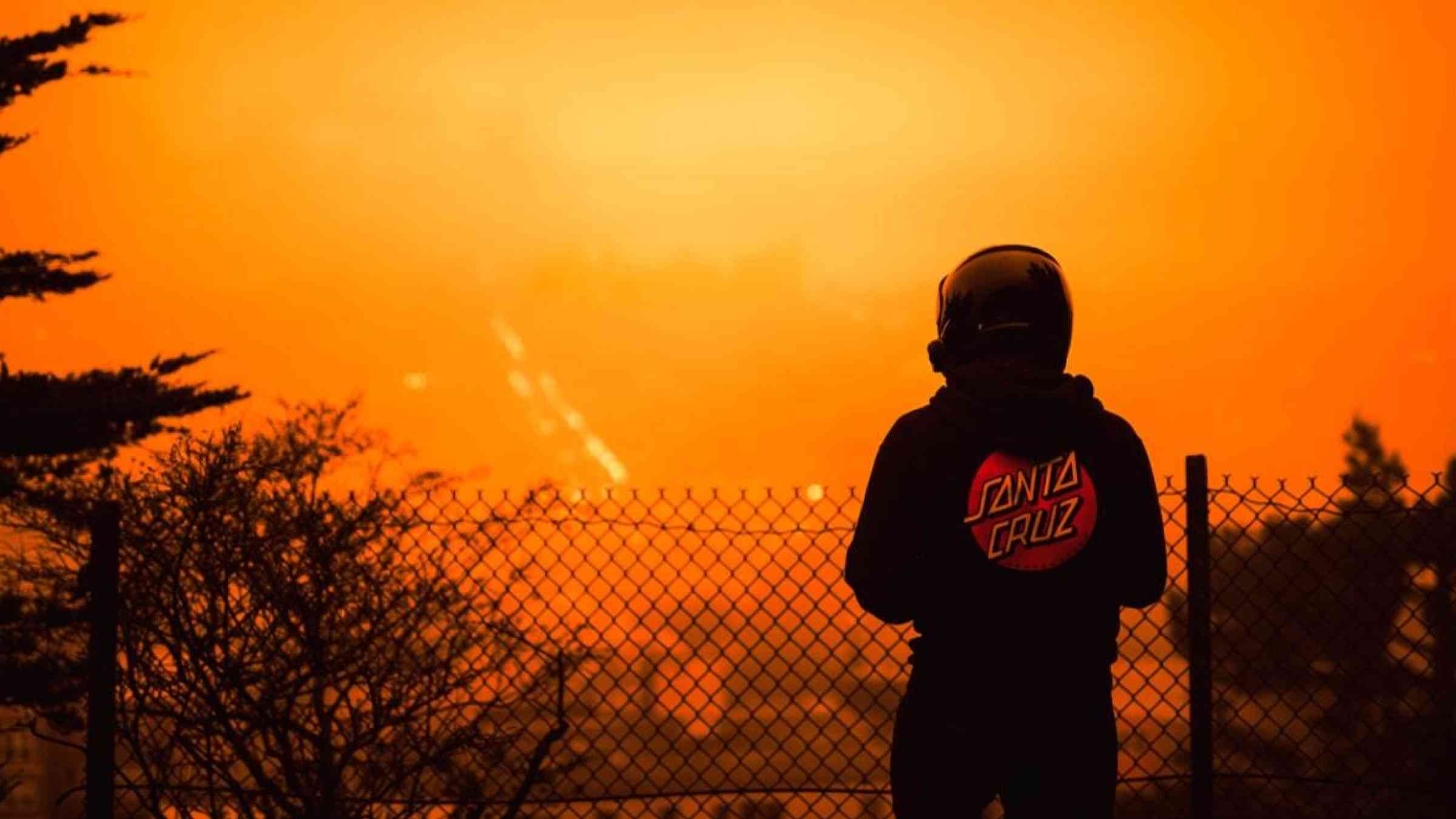 A man overlooks a wildfire visible from San Francisco under a hazy sky turned orange