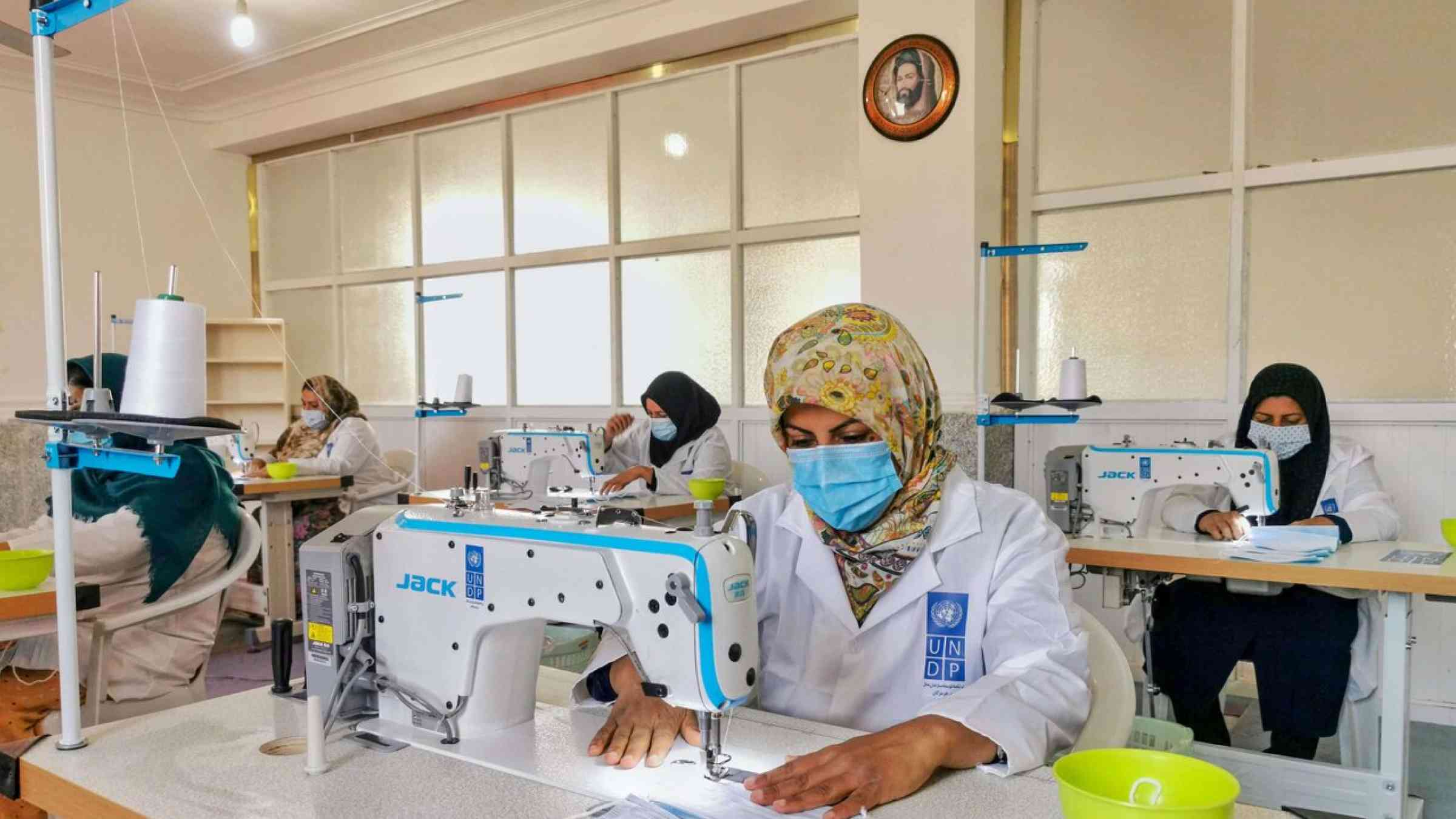 A photo of several women in lab coats and face masks making face masks in a UNDP workshop in Iran.