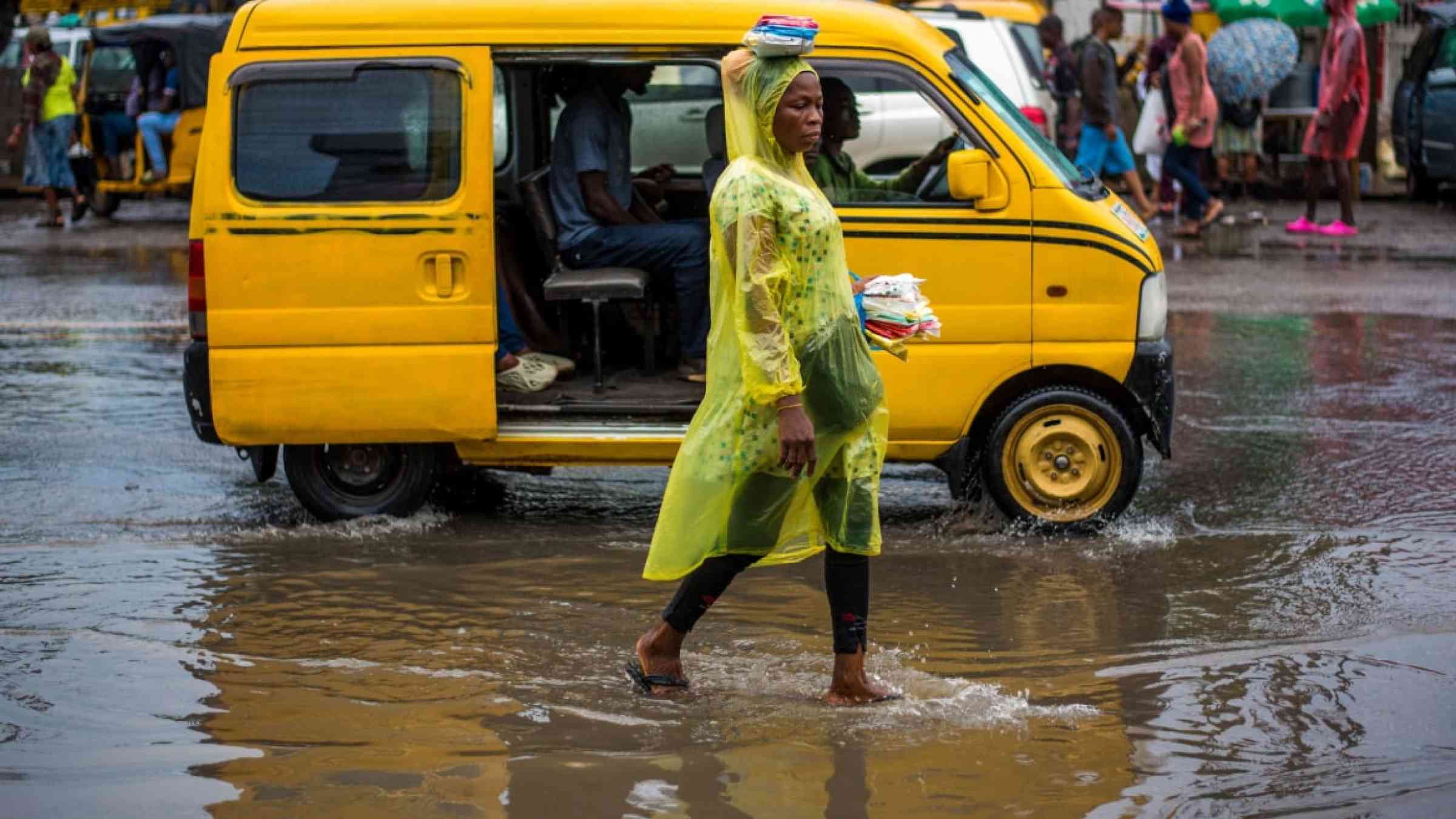 Woman walking through the flooded street in Nigeria with a yellow rain cape.
