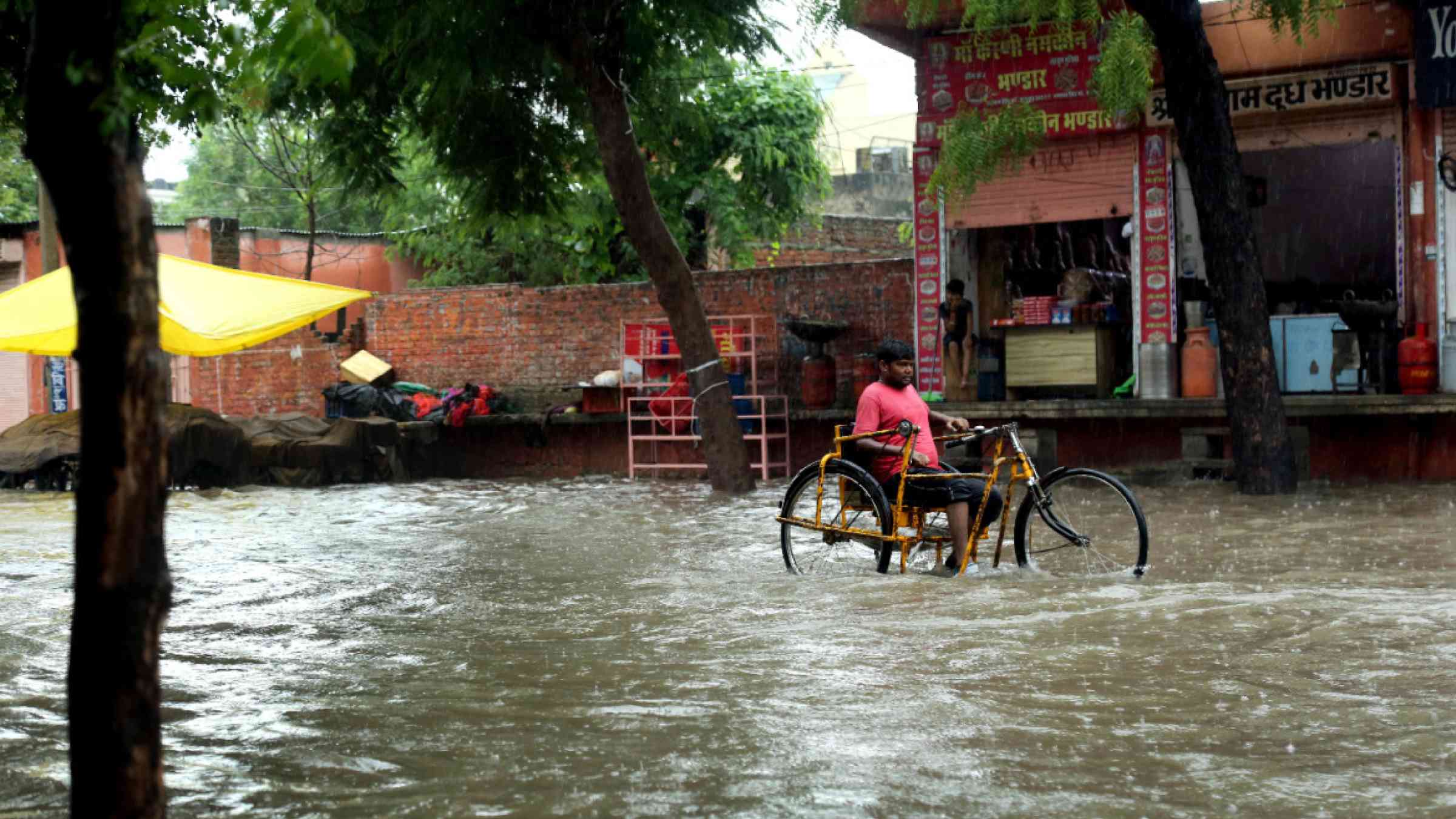 A disabled man wading through water logged road on his tricycle in India, 2020