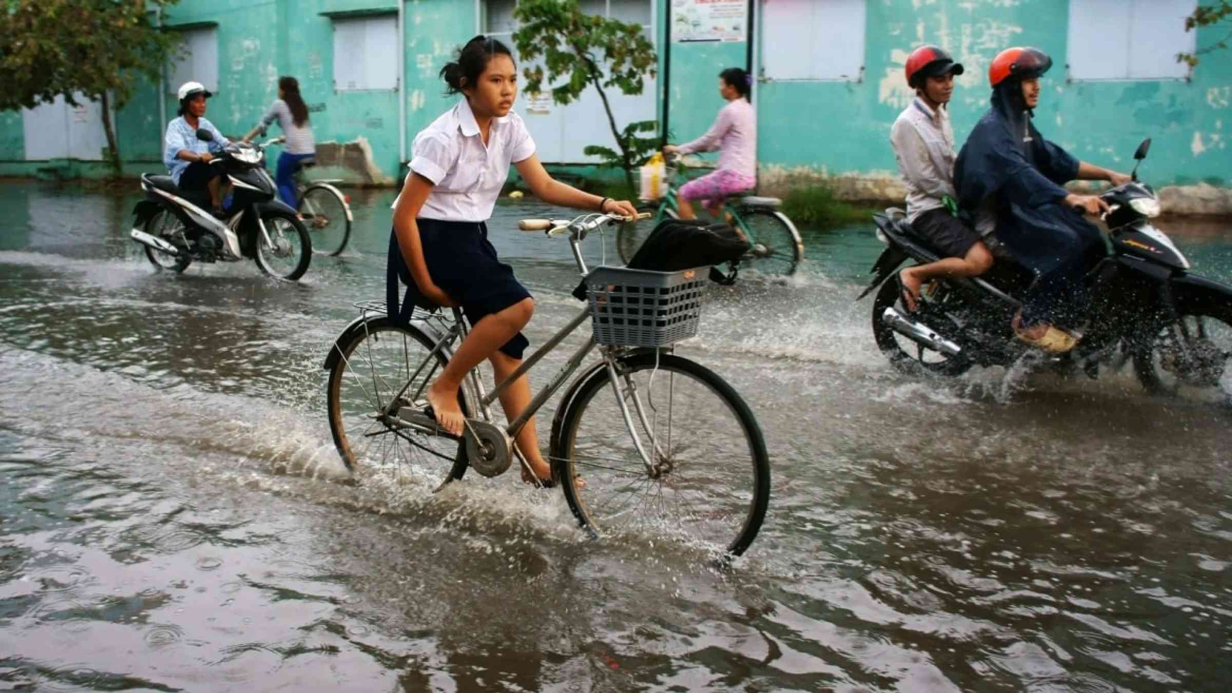 A Vietnamese school girl bikes through the flooded streets in Ho Chi Minh wearing her school uniform.