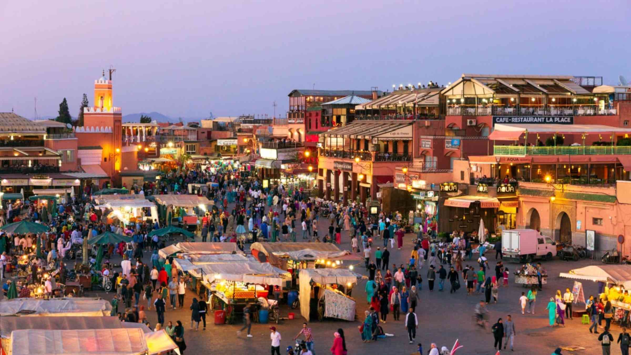 Tourists and locals on the Djemaa-el-Fna square during sunset in Marrakesh.
