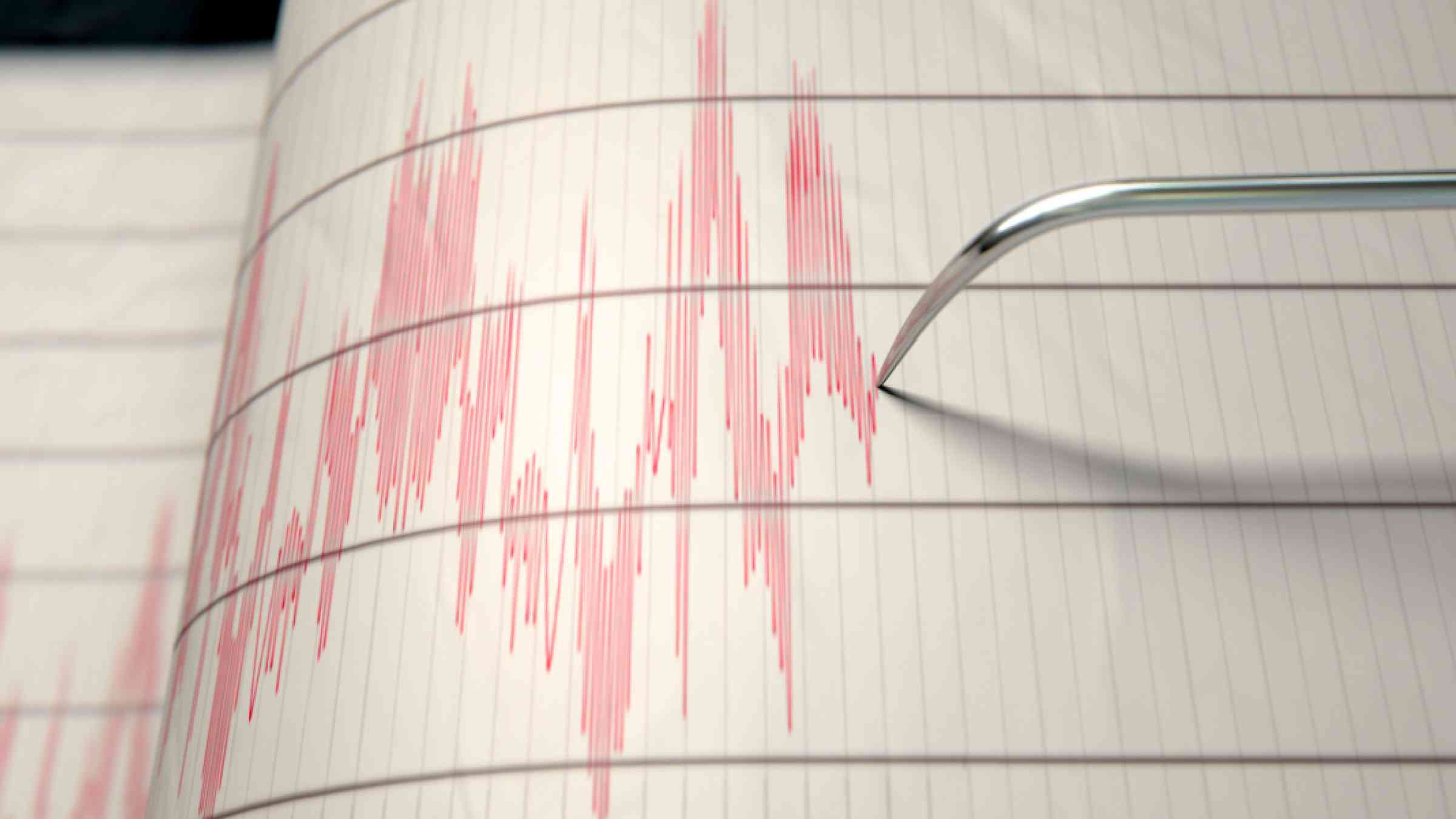 A closeup of a seismograph machine needle drawing a red line on graph paper