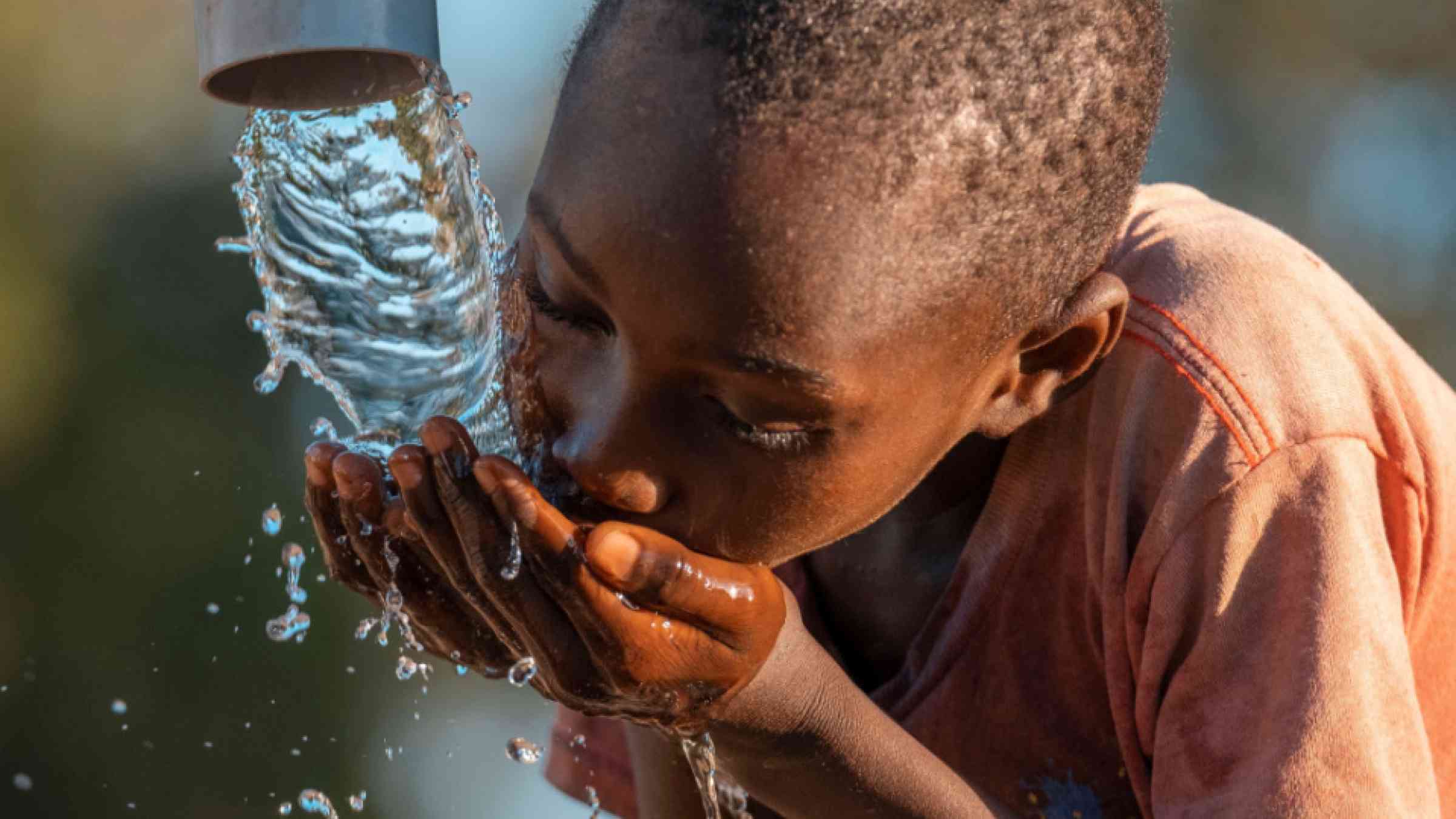 Happy boy drinking water from water pump, water fountain in village in Africa.