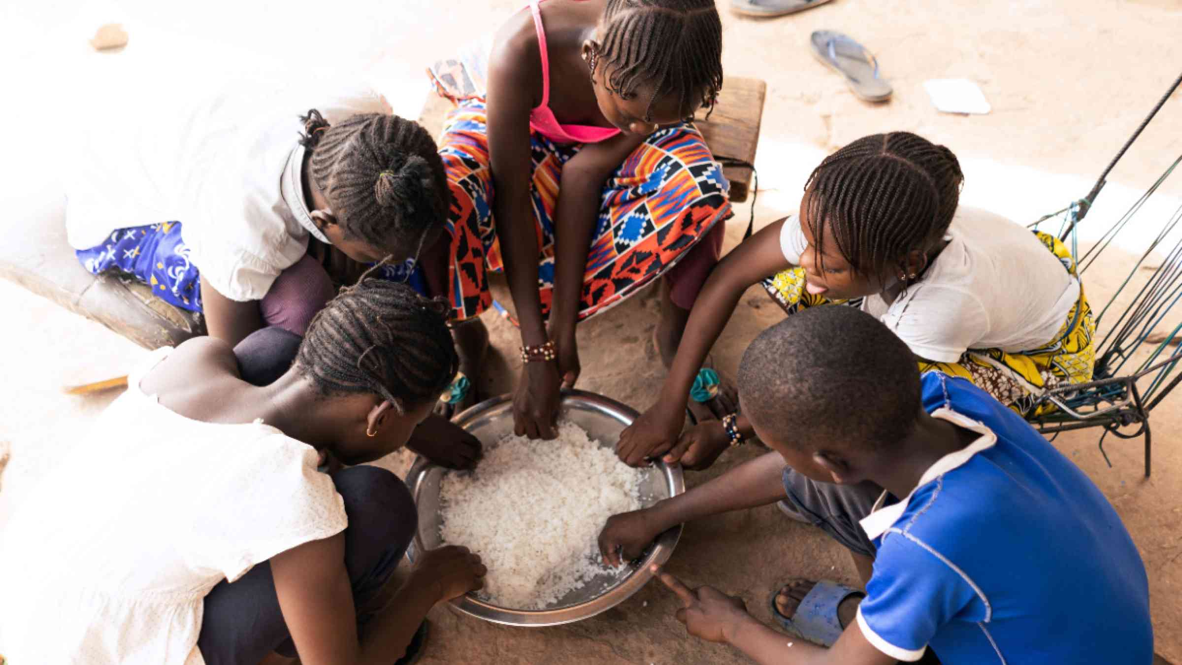 Group of children eating rice from a big shared bowl