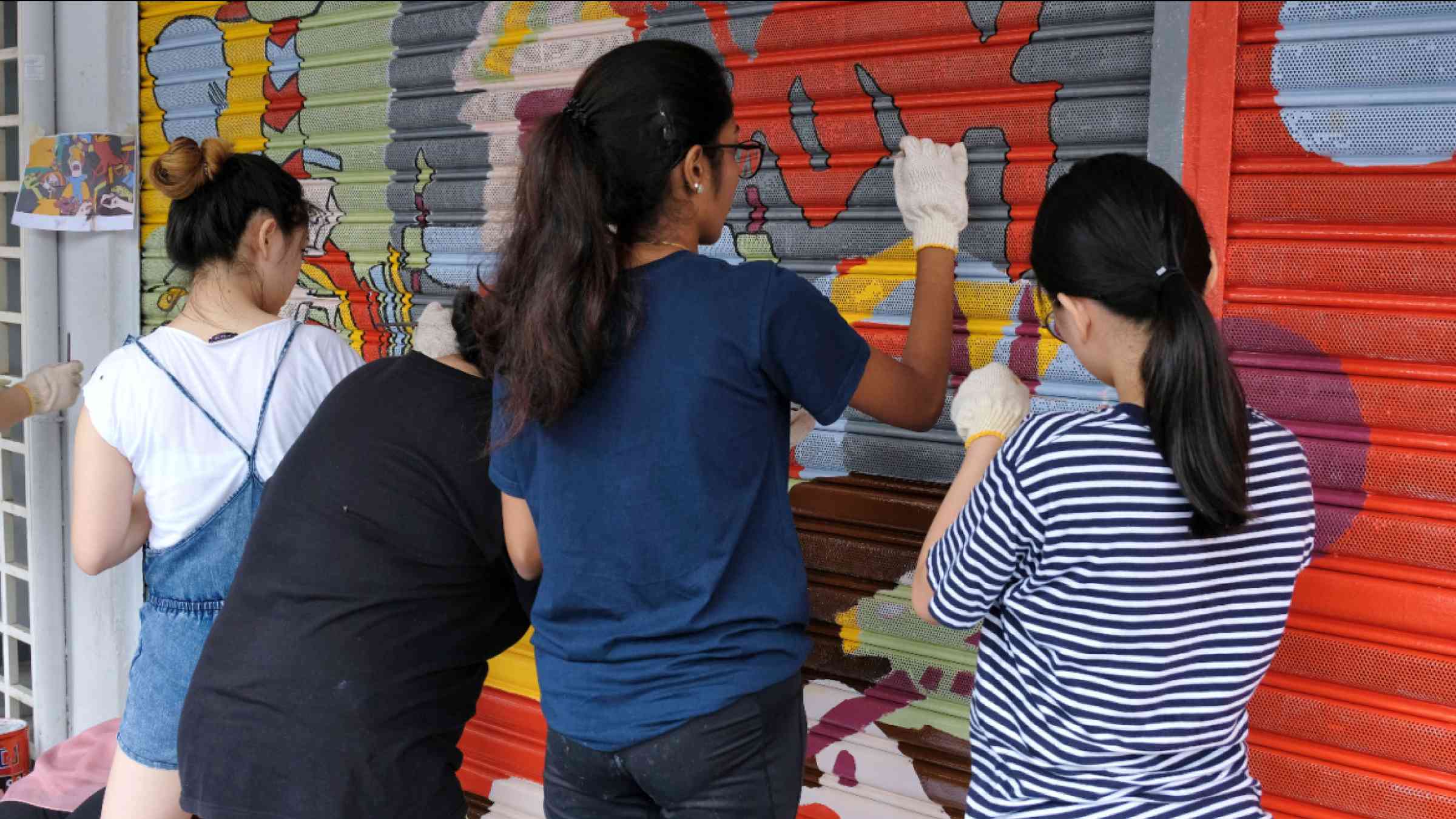 Street art takes shape as a volunteer group of young girls work together painting