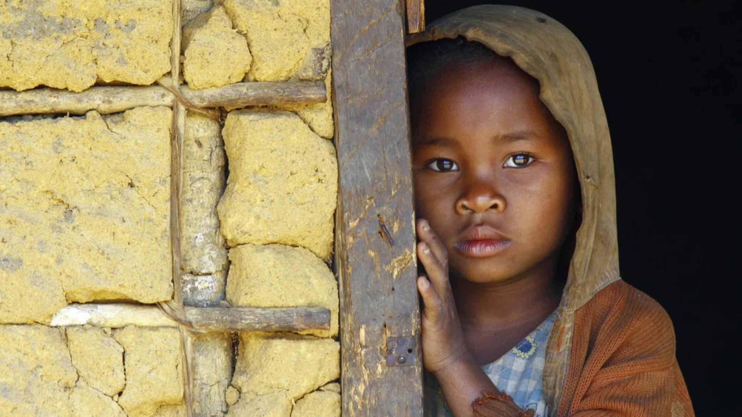 Young child standing inside the doorframe of a house in Madagascar, Africa.
