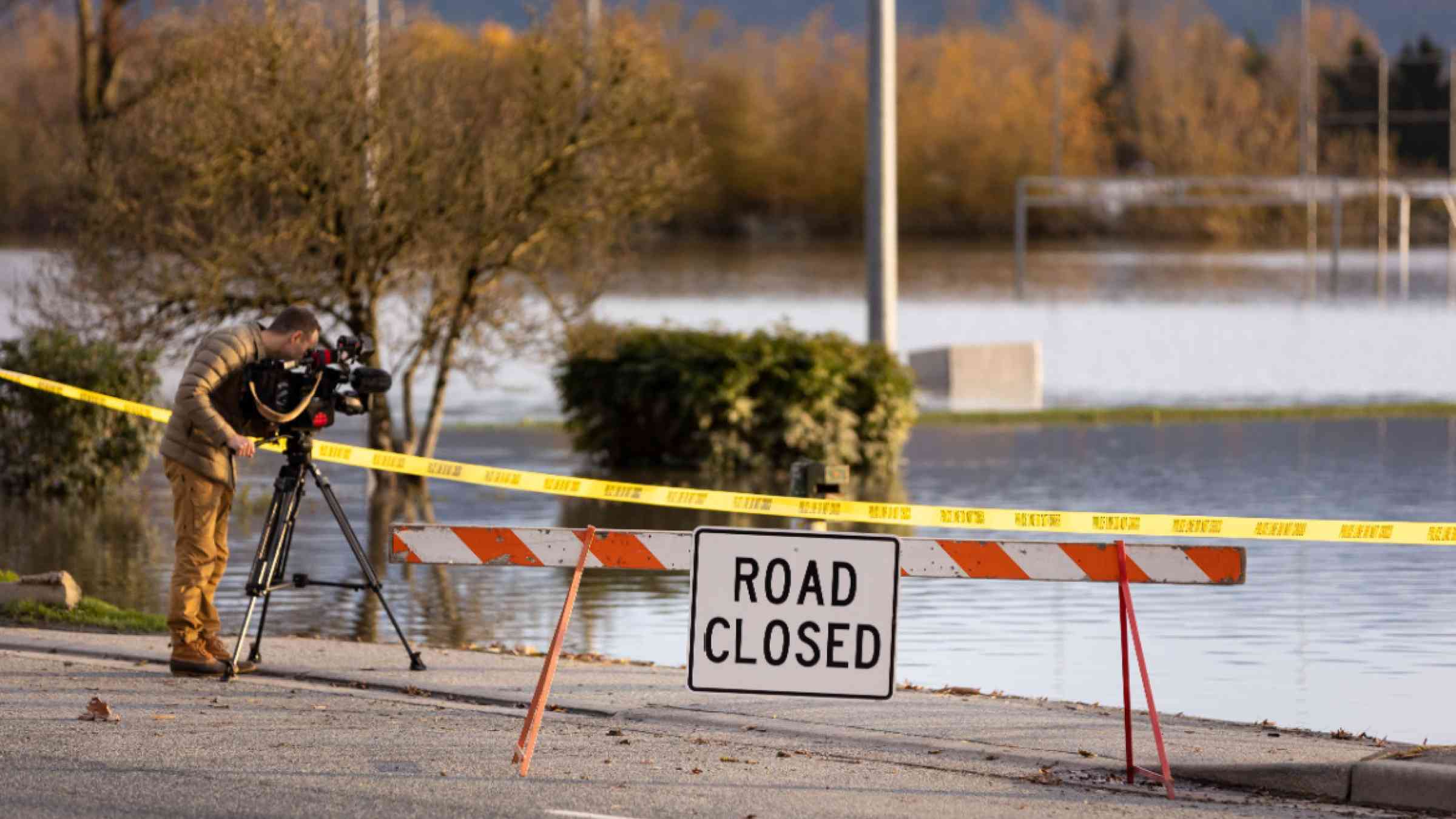 Journalist filming floods near a closed road signs due to infrastructure damage caused by heavy rain in the Fraser Valley, Canada in 2021