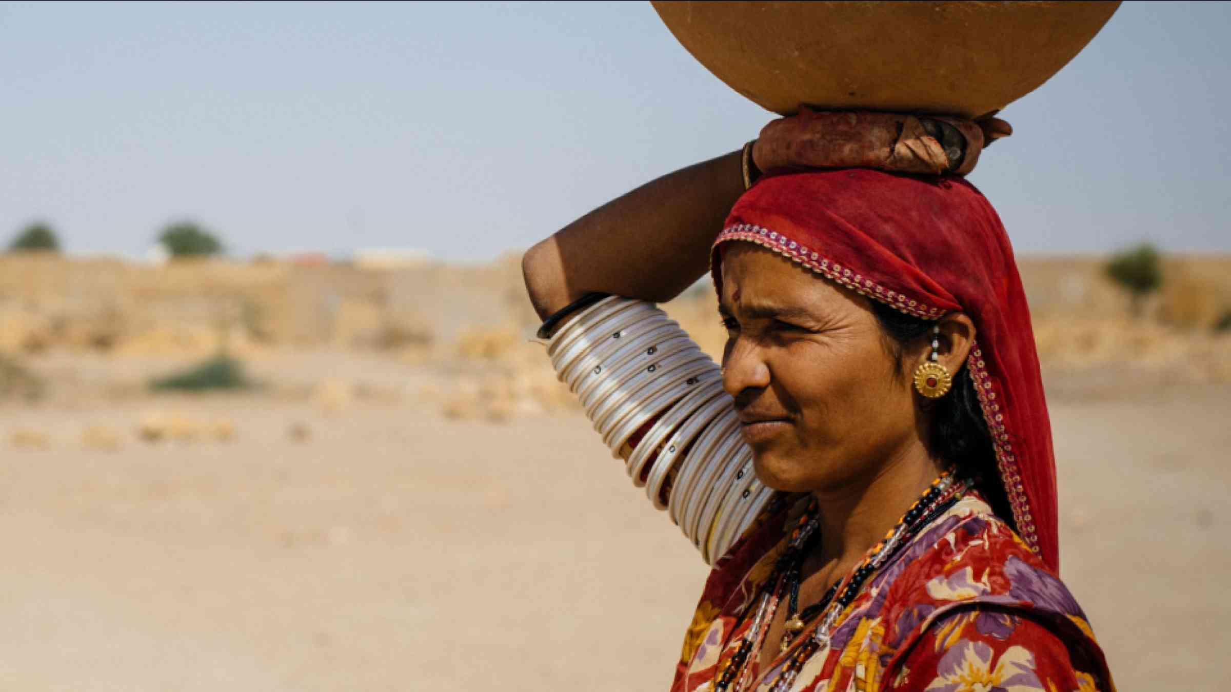 Indian woman holding a water recipient on her head in the desert