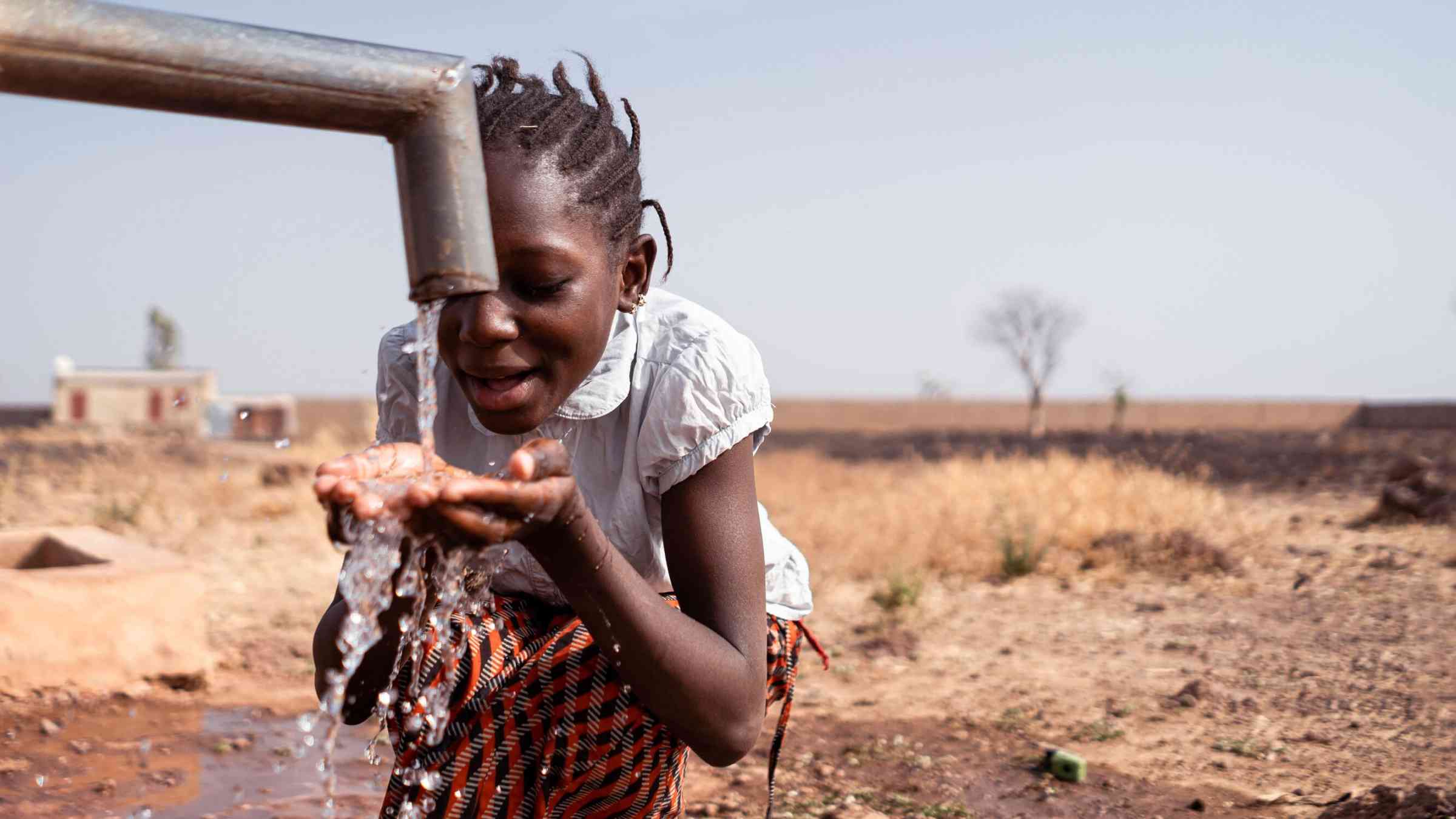 Young African girl drinking fresh water from a village tap