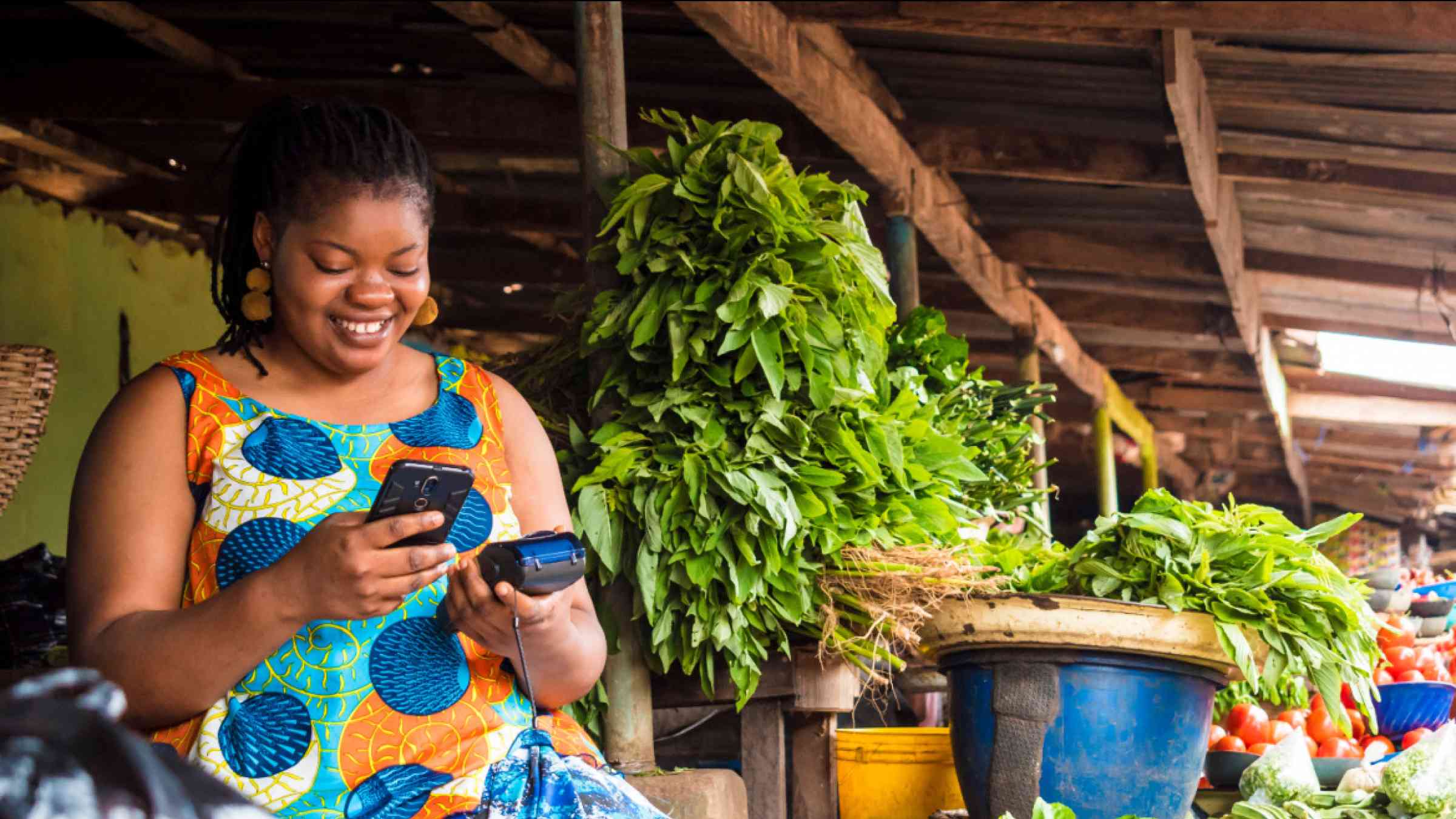African woman smiling and using her phone in a local market