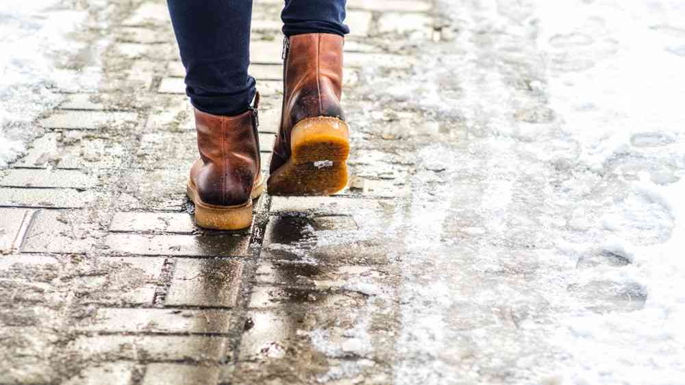 Walk on wet melted ice pavement. Back view on the feet of a man walking along the icy pavement. Pair of shoe on icy road in winter. Abstract empty blank winter weather background