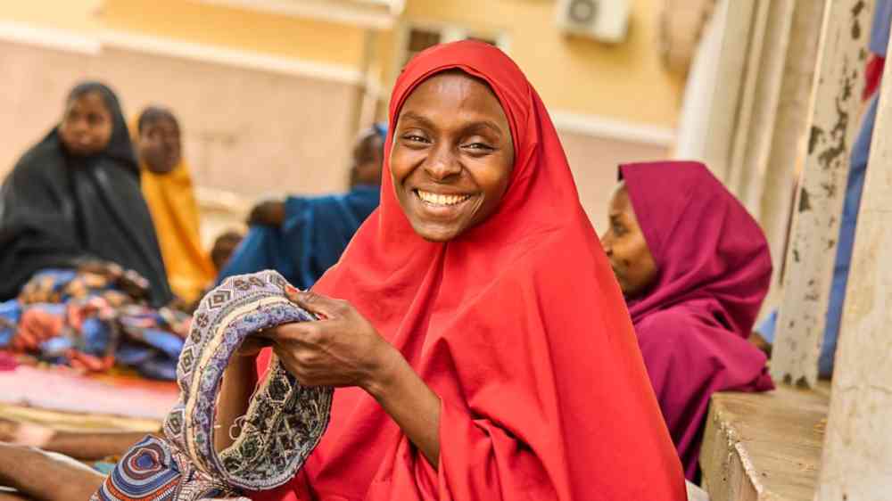 A breastfeeding mother knitting a cap while waiting to get her baby attended to at a stabilization center managed by International Rescue Committee in Bama local government area, Borno State, Nigeria