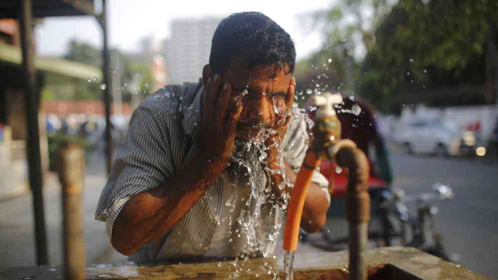 A man is wetting his face at a roadside tap to get relief from a heatwave in Dhaka