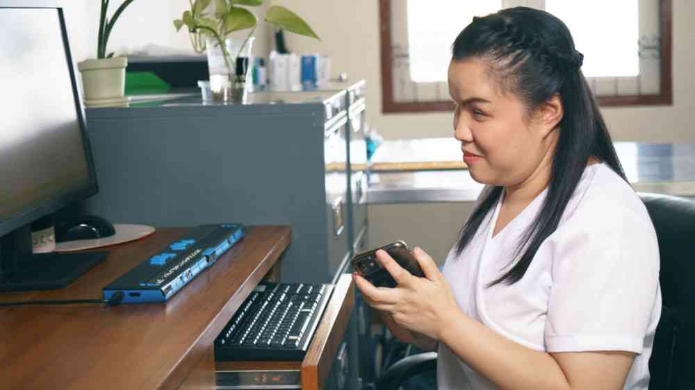 Woman with blindness disability using smart phone with voice accessibility in a workspace.