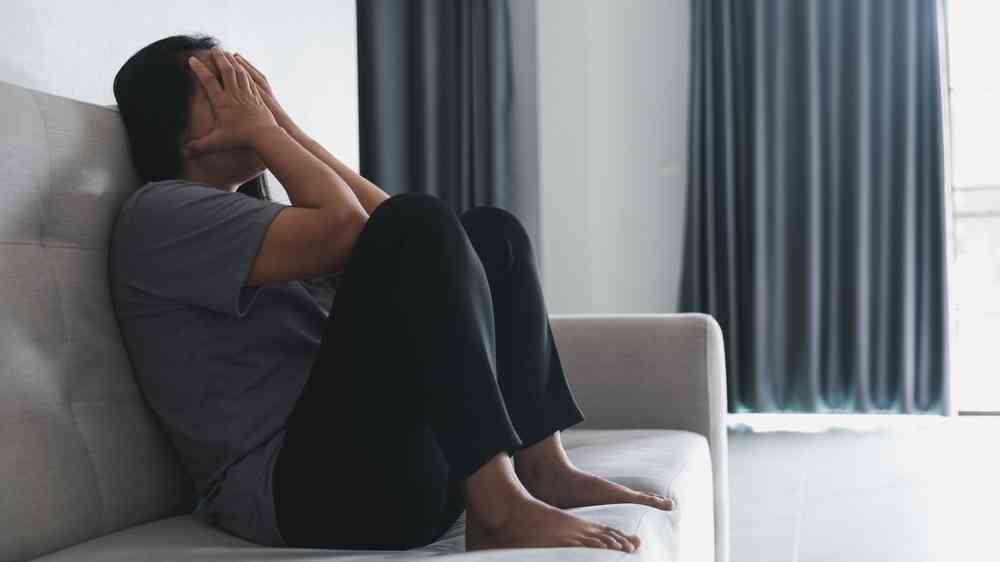 Depressed woman sitting against on sofa at home, mental health