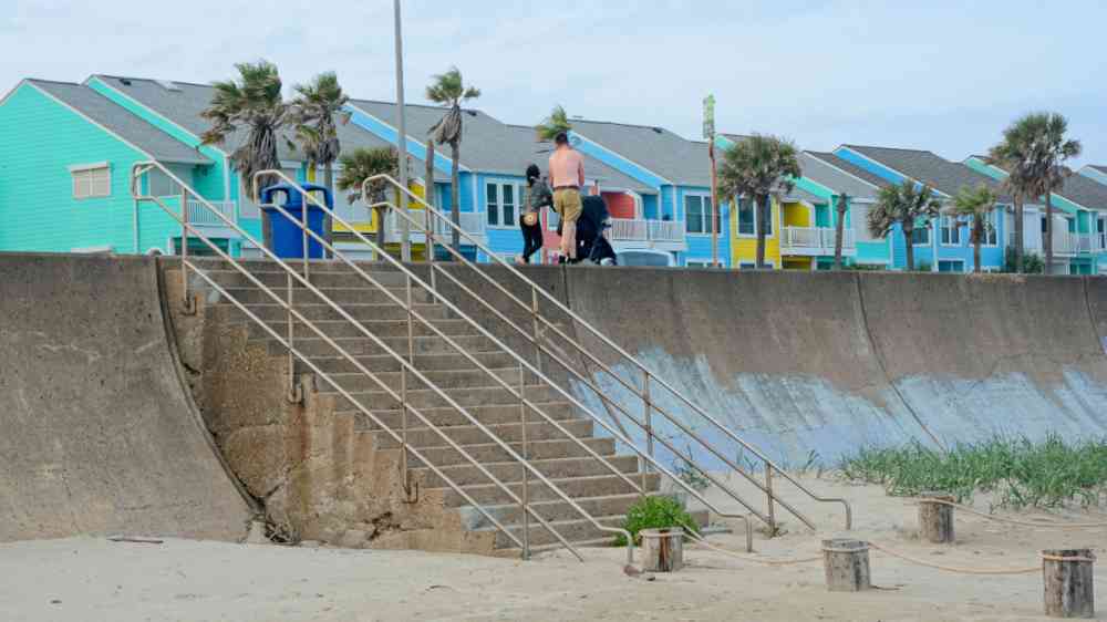 Young family strolling atop sea wall at Galveston (Texas, USA) beach past colorful row of houses. Concrete sea wall protects barrier Island from hurricane storm surge.
