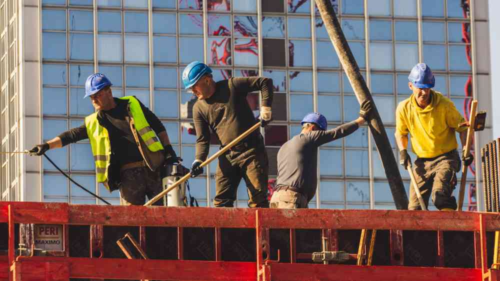 A group of construction workers in safety gear actively working on a high-rise building site.