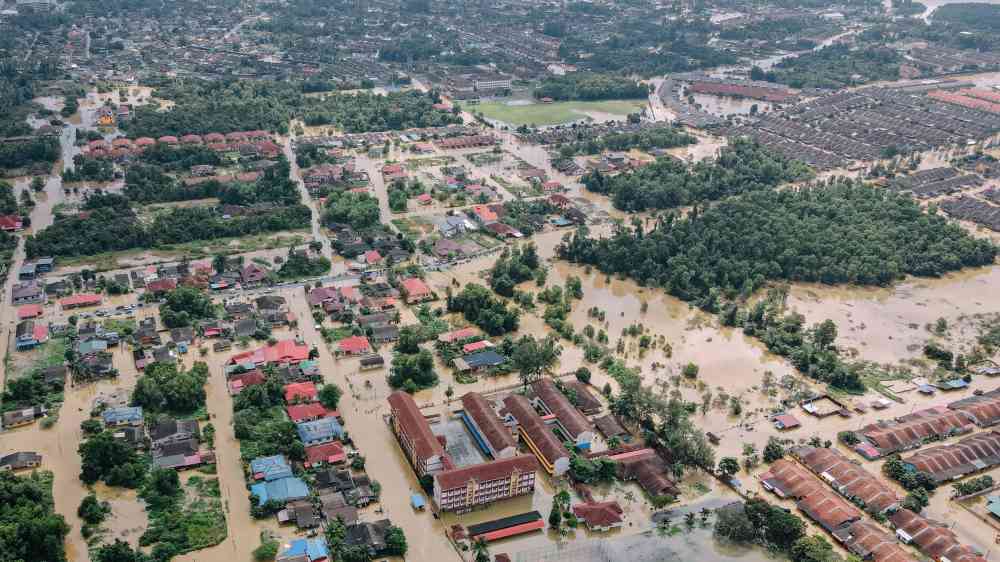 Aerial photograph capturing an extensive urban area affected by flooding, surrounded by lush green vegetation.