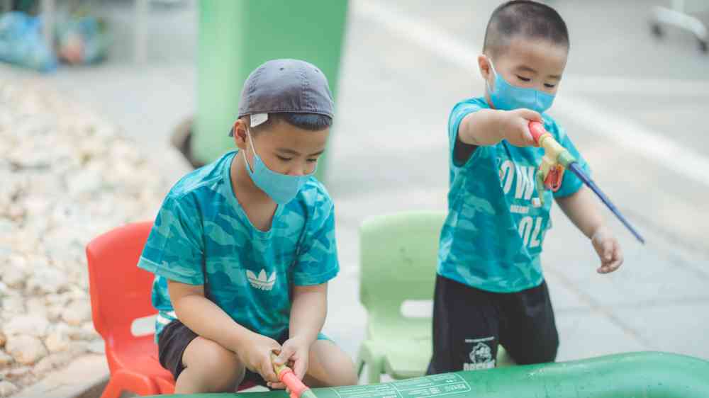 Two young boys in masks play with colorful toys outdoors
