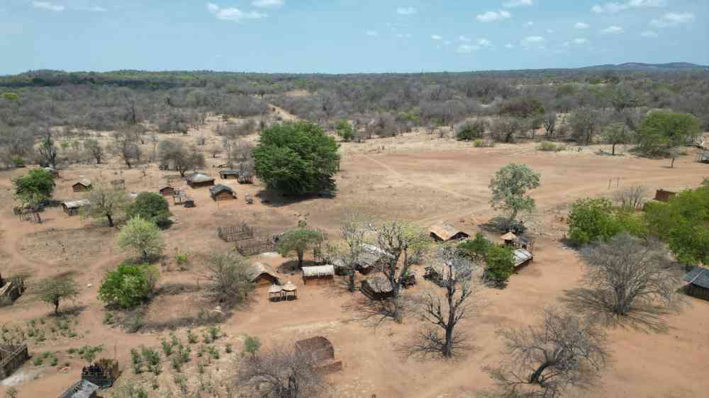 Aerial shot of a rural African village with traditional huts and sparse vegetation.