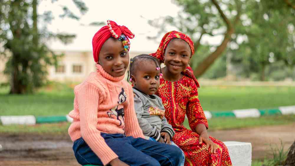 Three smiling children in vibrant clothing enjoying a sunny day outdoors.