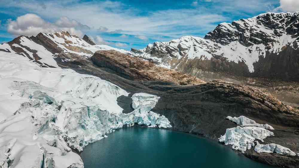 A breathtaking aerial view of the Andes with glaciers surrounding a turquoise lake under a vibrant blue sky.