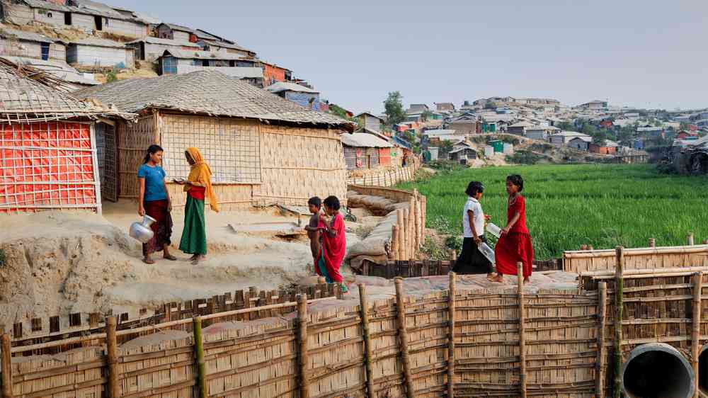 Refugees walk on an elevated footpath in Chakmakul camp, Teknaf. The footpath was built as part of monsoon preparedness initiatives, as the rice field below gets flooded in the monsoon. 