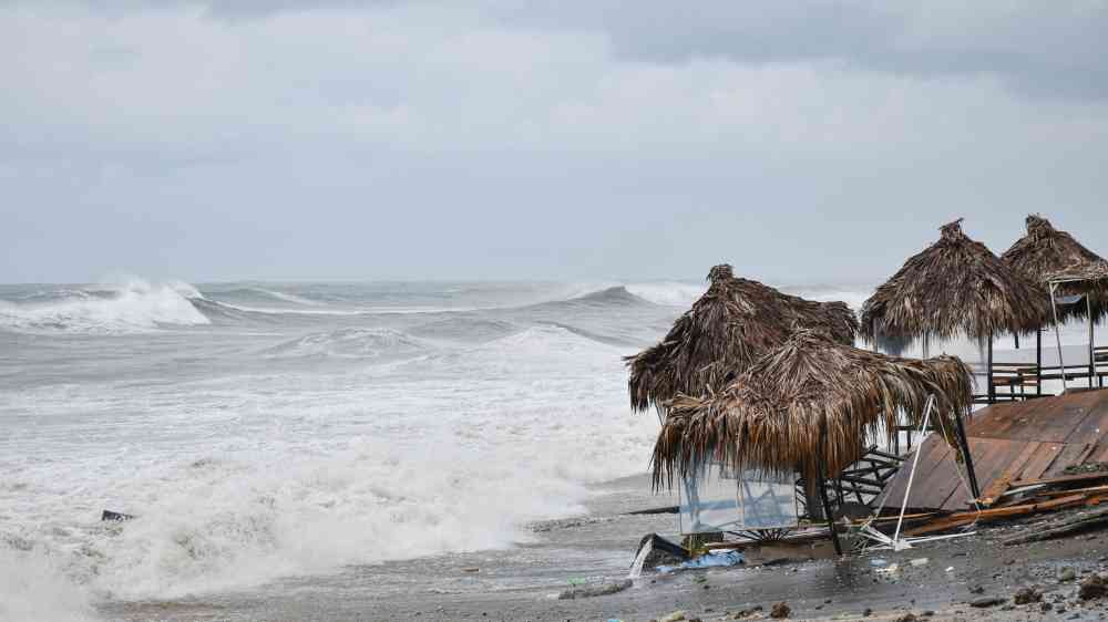 Dramatic waves crash on a Batumi beach with rustic huts under overcast skies.