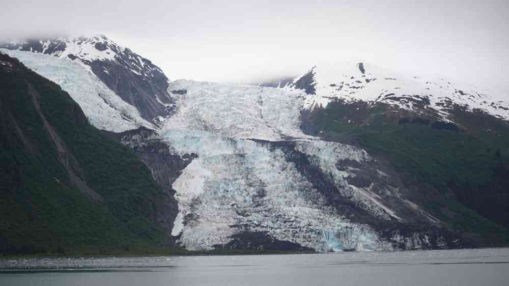 Majestic glacier flowing between snow-capped mountains by a serene lake in Alaska's pristine wilderness.