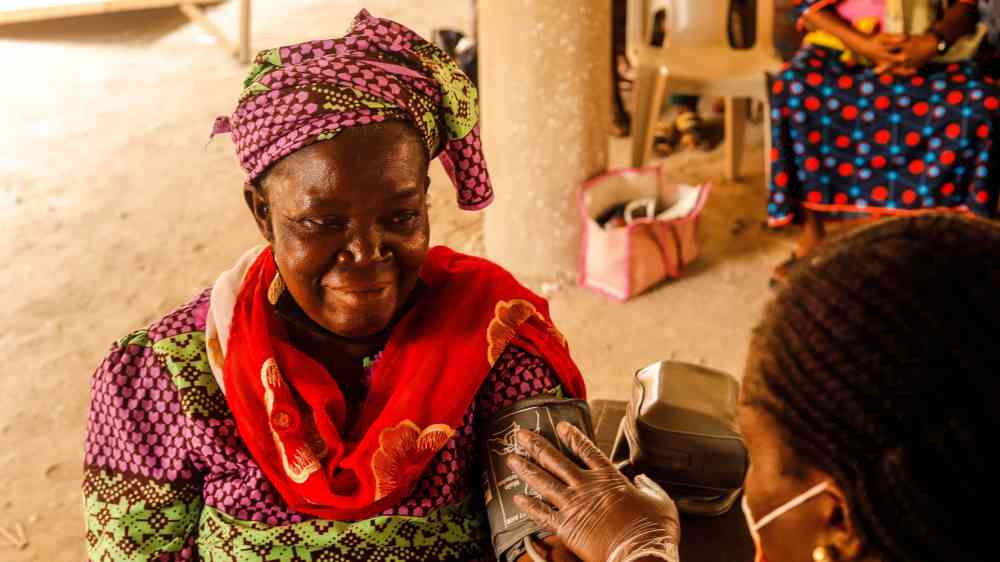 A smiling woman in traditional clothing having her blood pressure measured by a healthcare worker.