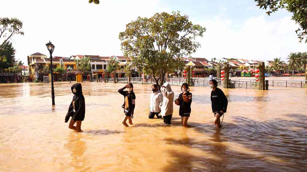 A group of people walking through floodwaters in an urban area, showcasing a natural disaster.