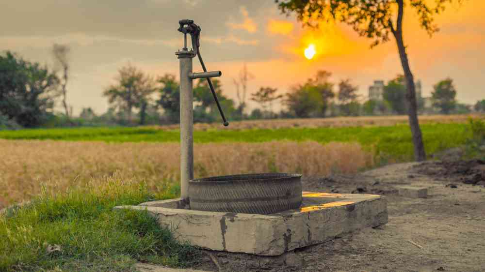 A vintage water pump amidst picturesque fields at sunset, capturing rural tranquility.