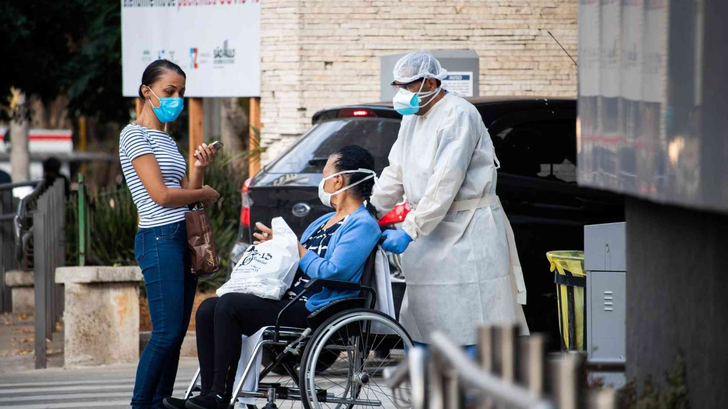 Picture of three people, a patient in a wheelchair, a doctor and one more person exiting a hospital.