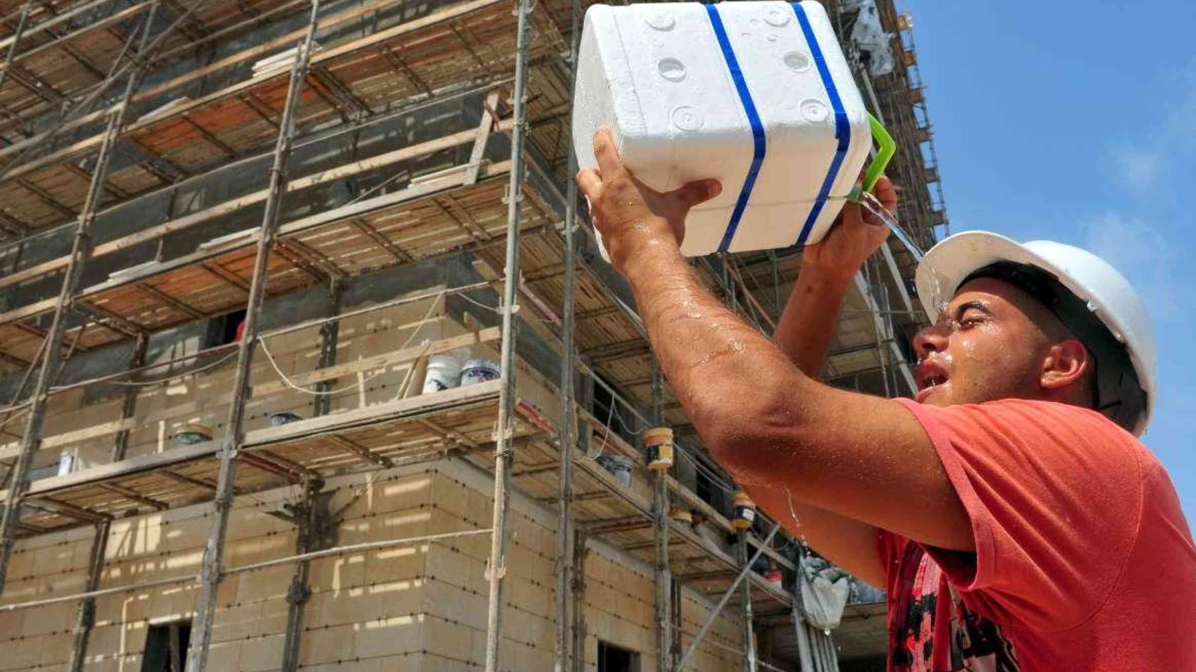 A builder cooling down with cold water during heat wave. ChameleonsEye / Shutterstock.com