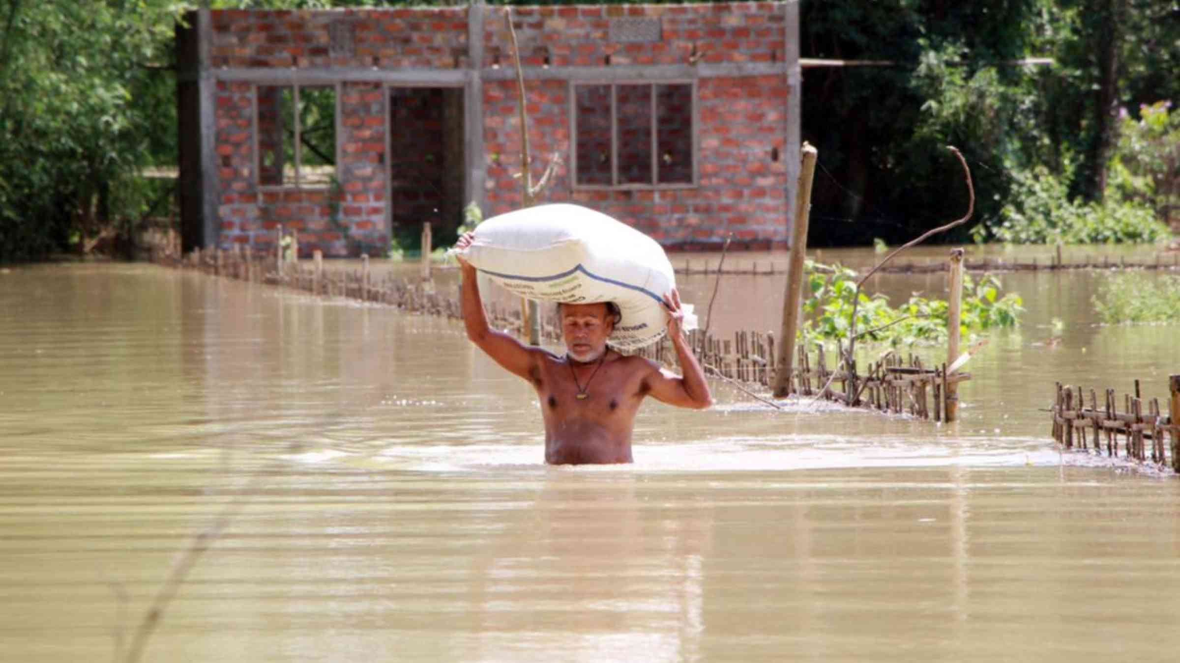 A man shifting his food grains to the high land as the flood water submerged his house in Assam, India (May 2020). Simanta Talukdar/Shutterstock