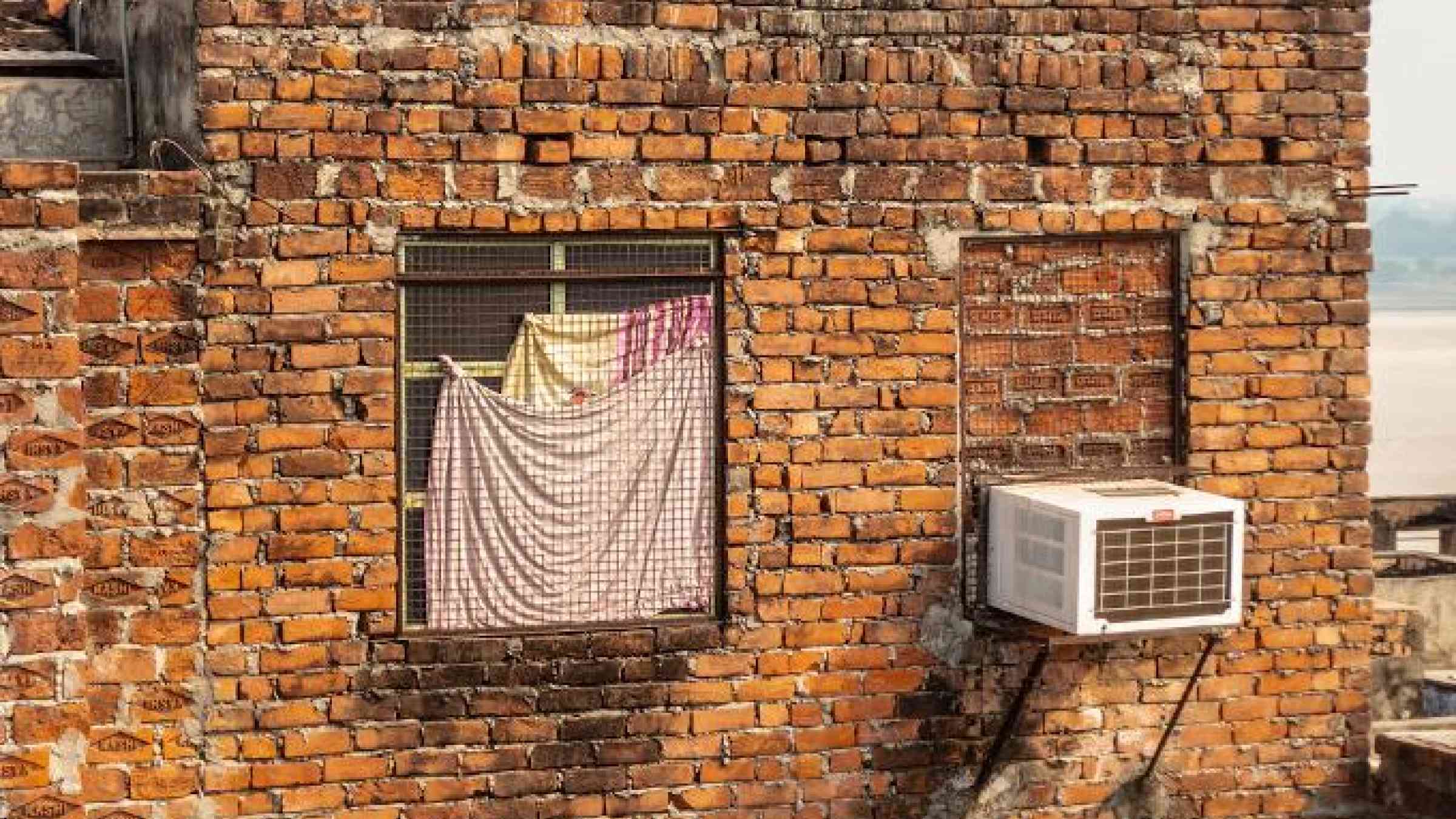 Varanasi, Uttar Pradesh, India: Bare, brown brick walls of a house with a mesh window and an air conditioner. balajisrinivasan/Shutterstock