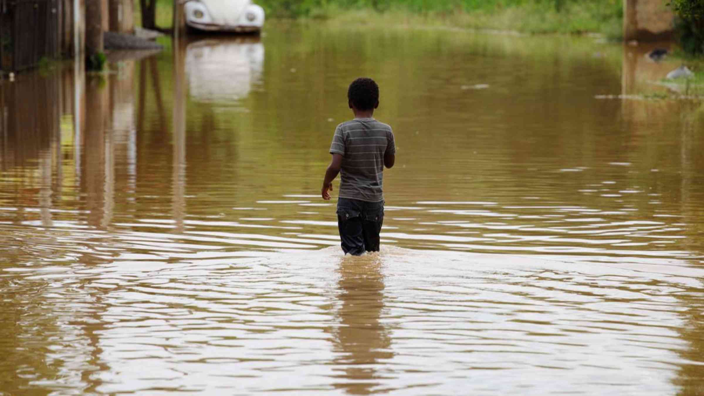 A young boy looks on as he walks through a flooded street after heavy rains hit a residential neighborhood in Capivari, Brazil (2015). Nelson Antoine/Shutterstock
