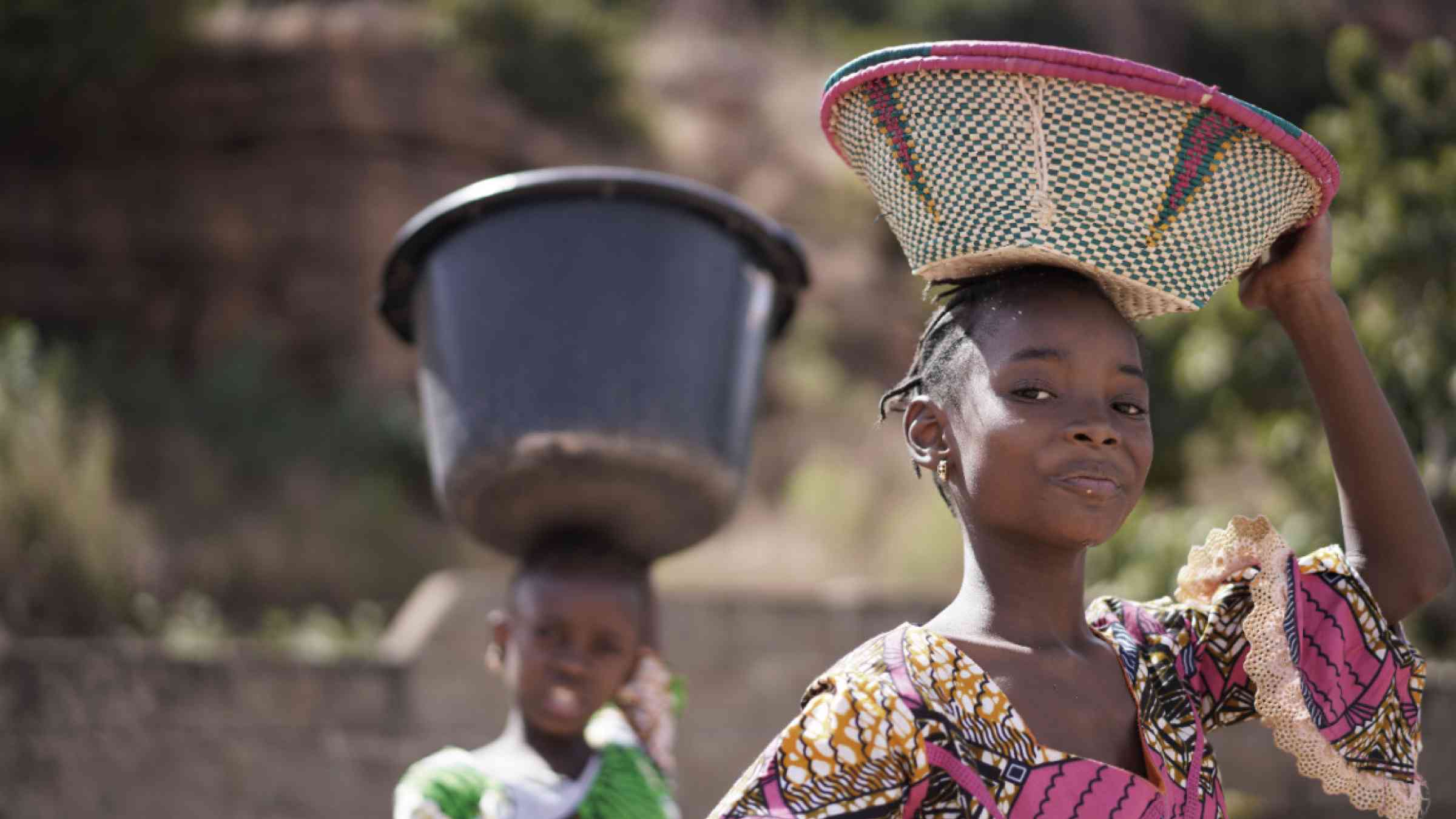 Two proud African girls carrying heavy household items on their head