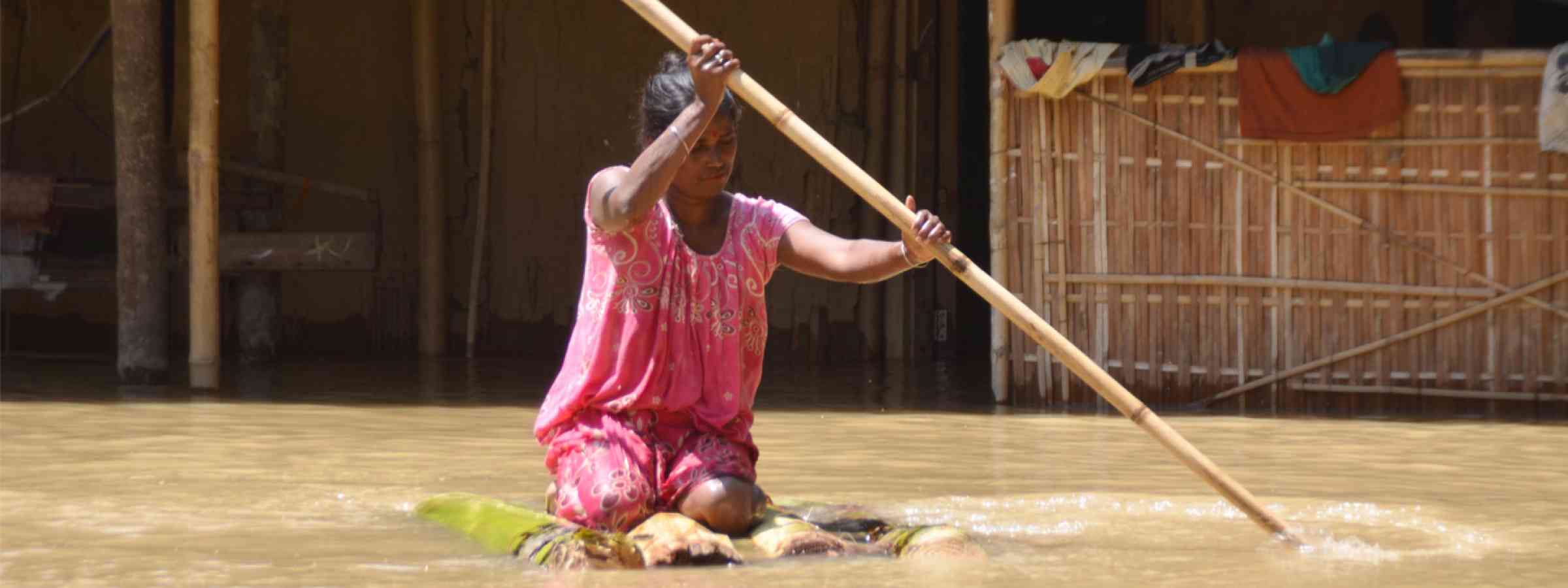 A woman in Assam, India paddles through flooded water using a makeshift raft (2020)