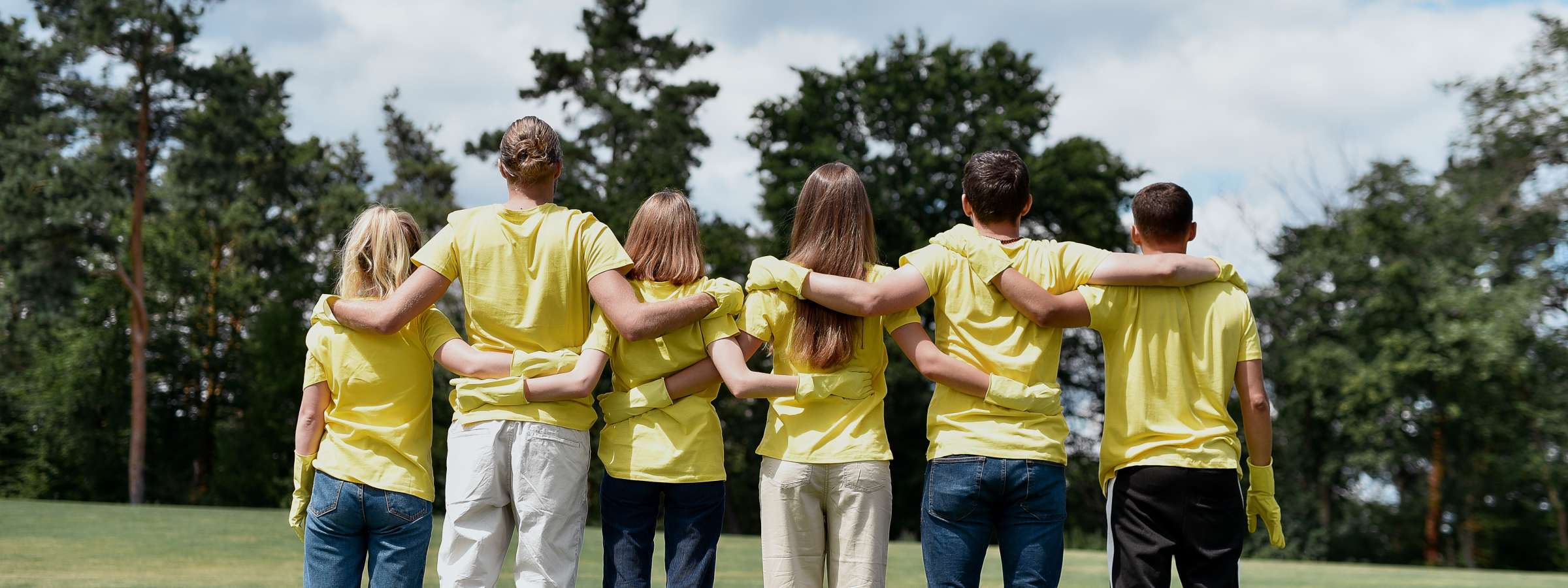 Group of young people facing a forest and hugging each other