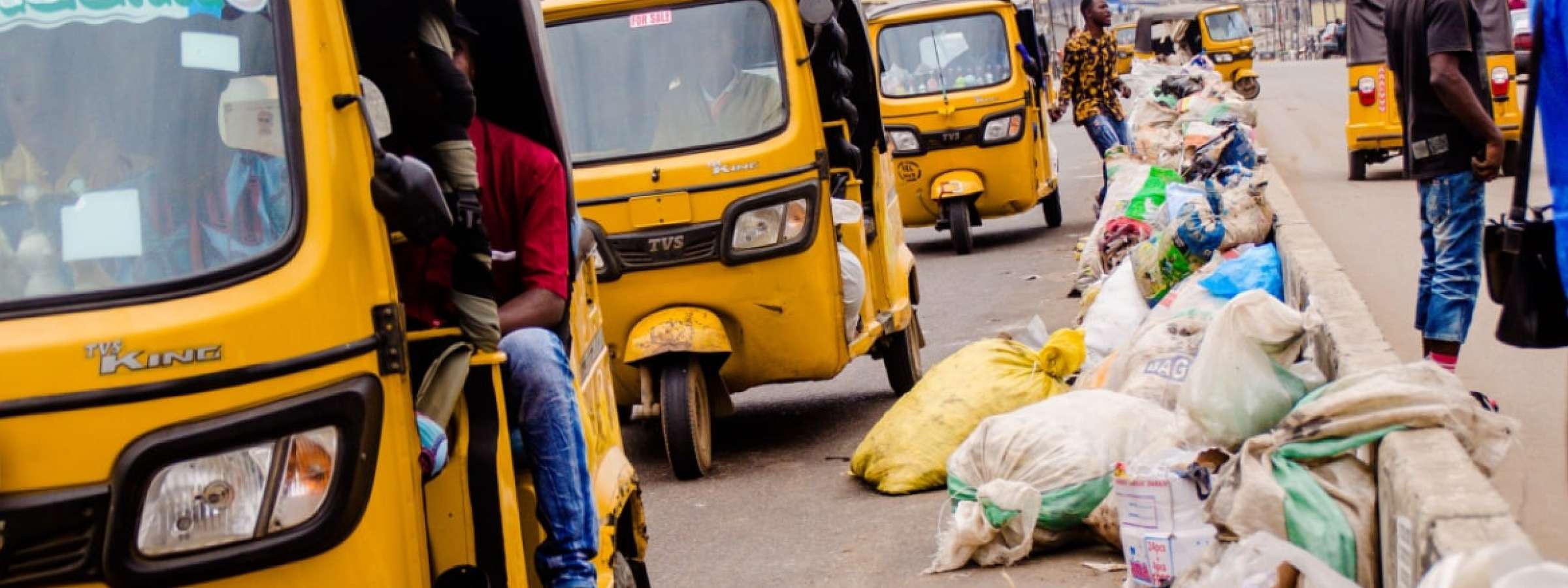 Waste laying on the streets in Nigeria. Yellow tricycles pass the waste along the road.