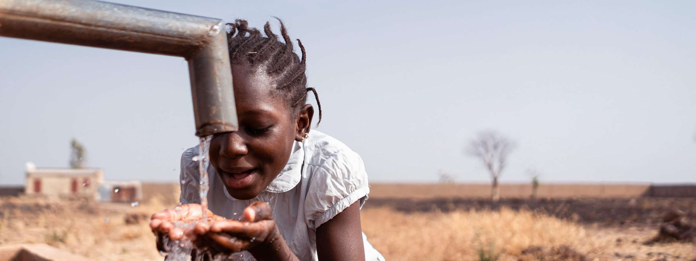 Young African girl drinking fresh water from a village tap